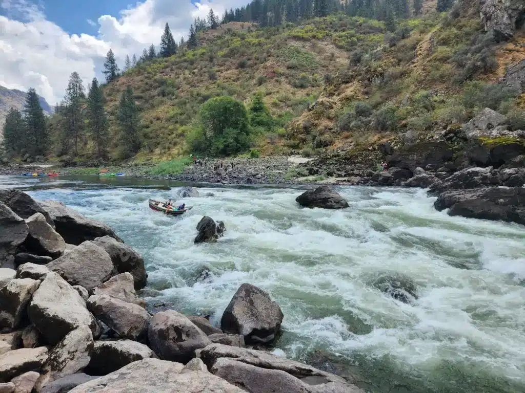 River rafting adventure: Boat navigates rapids surrounded by rocks and a forested hillside.