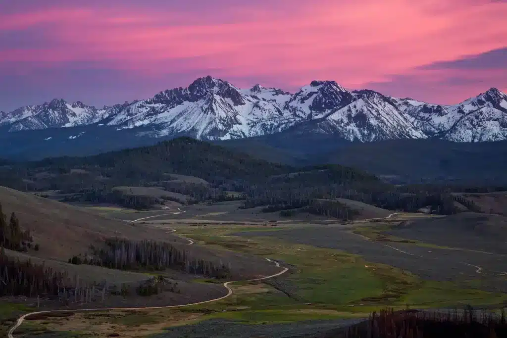 Scenic mountain landscape at sunset, snow-capped peaks, winding trail, panoramic view, outdoor adventure, nature photography.