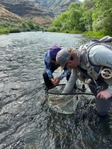 Flyfishing in Boise: Two anglers netting a fish in a river, surrounded by a mountain landscape. Flyfishing image gallery.
