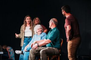 Enthusiastic group in Assemblage Boise improv class. People laughing, interacting on stage, enjoying comedic performance.