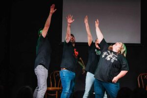 Enthusiastic improv class performers with hands raised on stage at Assemblage Boise. Learn improv comedy today!