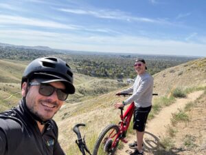 Mountain biking clinic in Boise: Two cyclists pause on trail with a scenic city view behind them. Boise mountain biking.