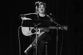 Assemble Boise: Woman performing live music with acoustic guitar and microphone at a music experience event.