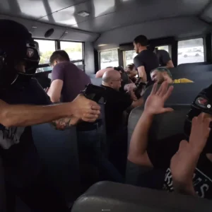 Tactical Training: Team assemble inside bus, simulating a hostage situation. Gun pointed, high stress environment.