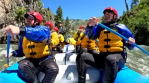 Whitewater rafting adventure in Boise, Idaho. Team paddling down river in raft, wearing helmets and life jackets.