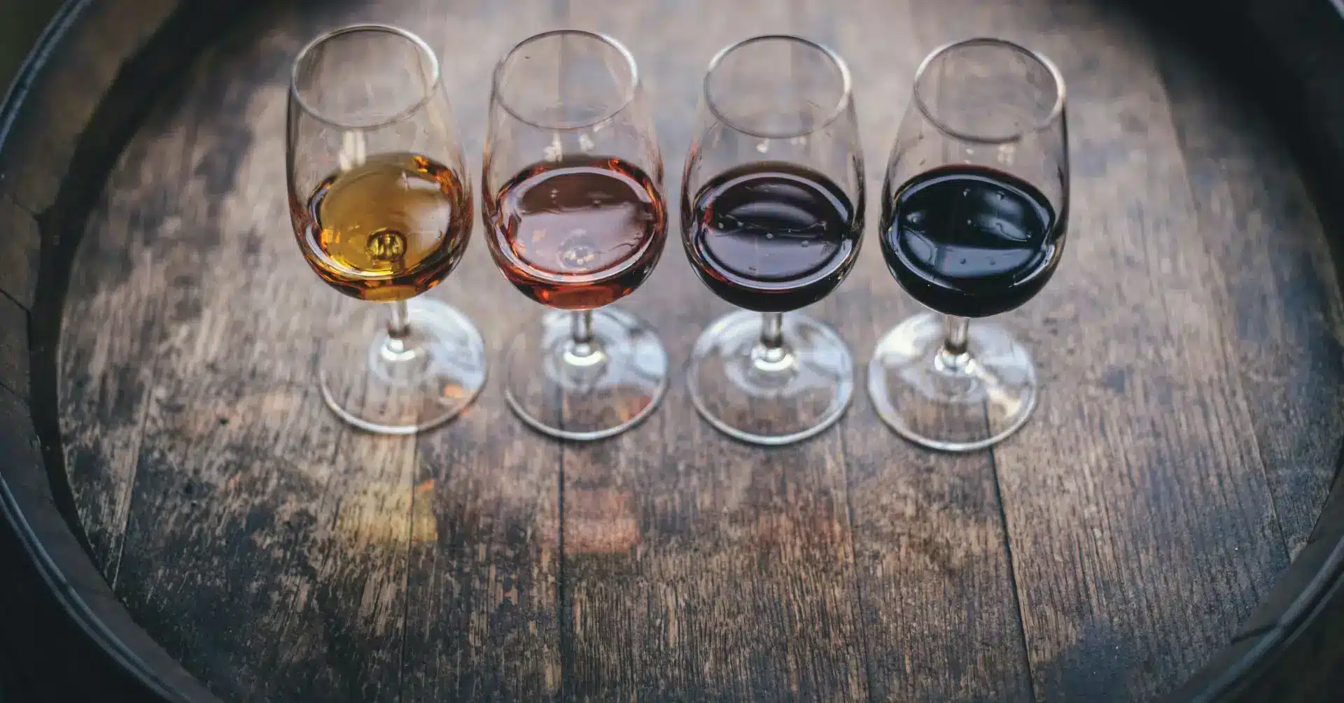 Wine education: Four glasses of different wines on a wooden barrel in Boise, ideal for wine tasting and learning.